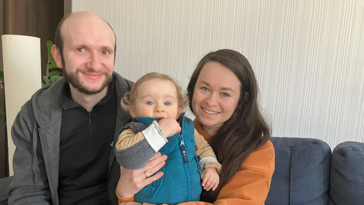 伊霍尔与尤利娅抱着儿子，三人坐在简陋家具中