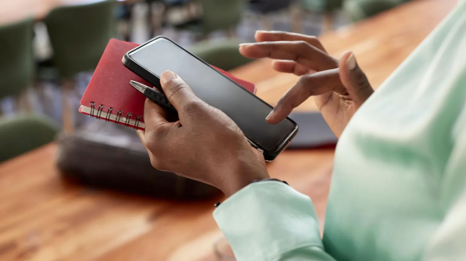 一名女性手持笔记本和笔，同时操作手机